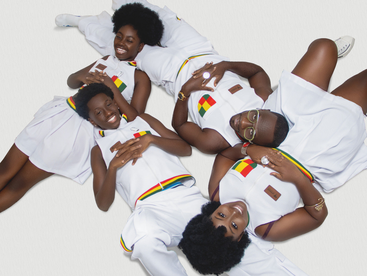 Okyeame Kwame and family in matching sleeveless white jersey outfits, featuring bold splashes of red-gold-and-green.