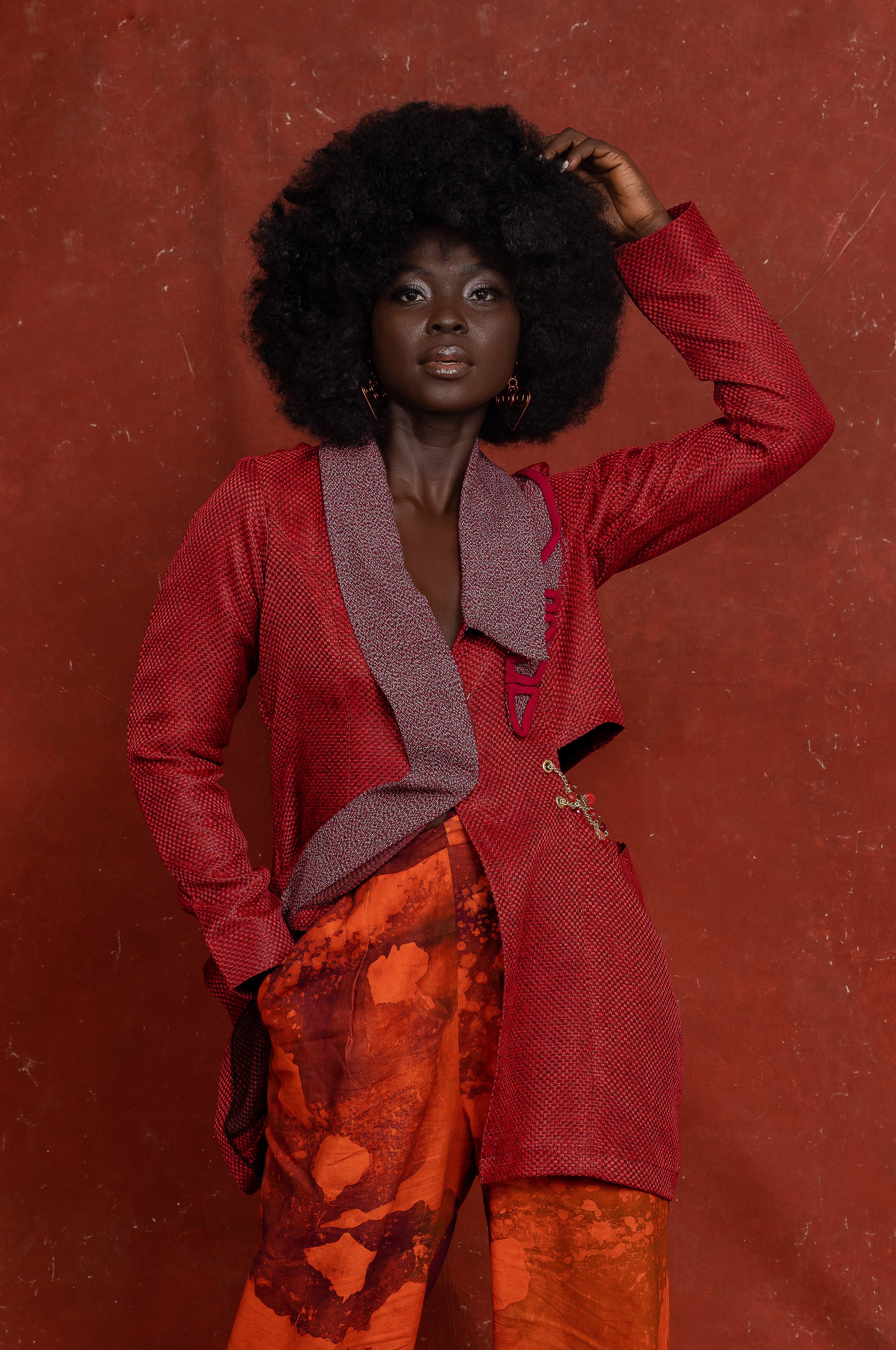 Person wearing a red coat and orange pants against a red background